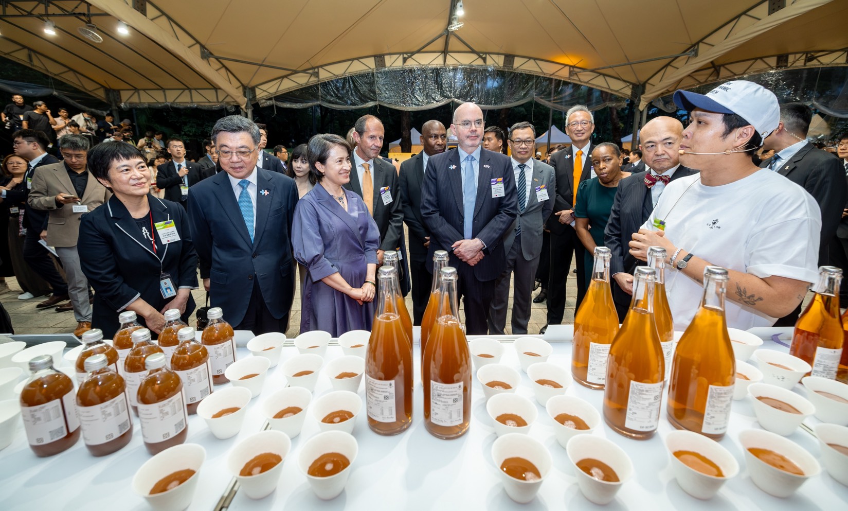 圖說六:外交部政務次長吳志中(右三)、政務次長陳明祺(右四)陪同蕭美琴副總統(左三)、行政院長卓榮泰(左二)、使節暨駐台代表團聆聽「仃杉實驗室」工作人員介紹茶酒及氣泡茶。(照片來源:總統府)