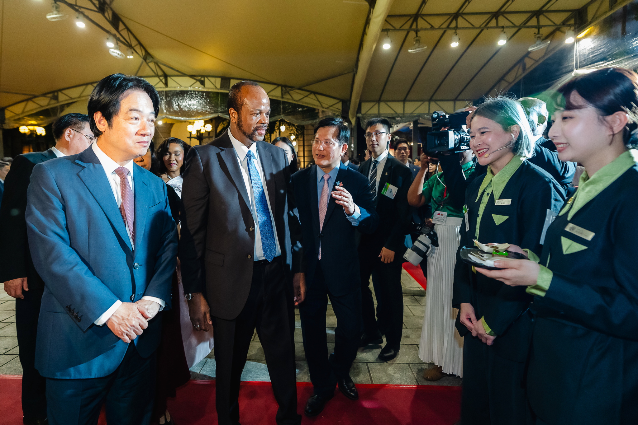 圖說二:外交部長林佳龍(右一)陪同賴清德總統(左一)、國安會秘書長吳釗燮(後排左)與史瓦帝尼國王恩史瓦帝三世陛下(H.M. King Mswati Ⅲ,中)暨祖瑪王妃殿下(Inkhosikati Make Zuma,後排右)至「心潮飯店」攤位聆聽焰香鴨肉羹、三杯雞飯捲等創意料理介紹。